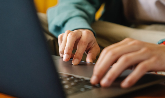 Detaljbild på två händer som skriver på tangentbordet på en laptop.