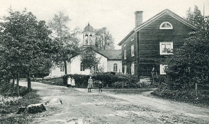 Äldre svartvit fotografi med vägen och kyrkan. Några barn går på vägen. 