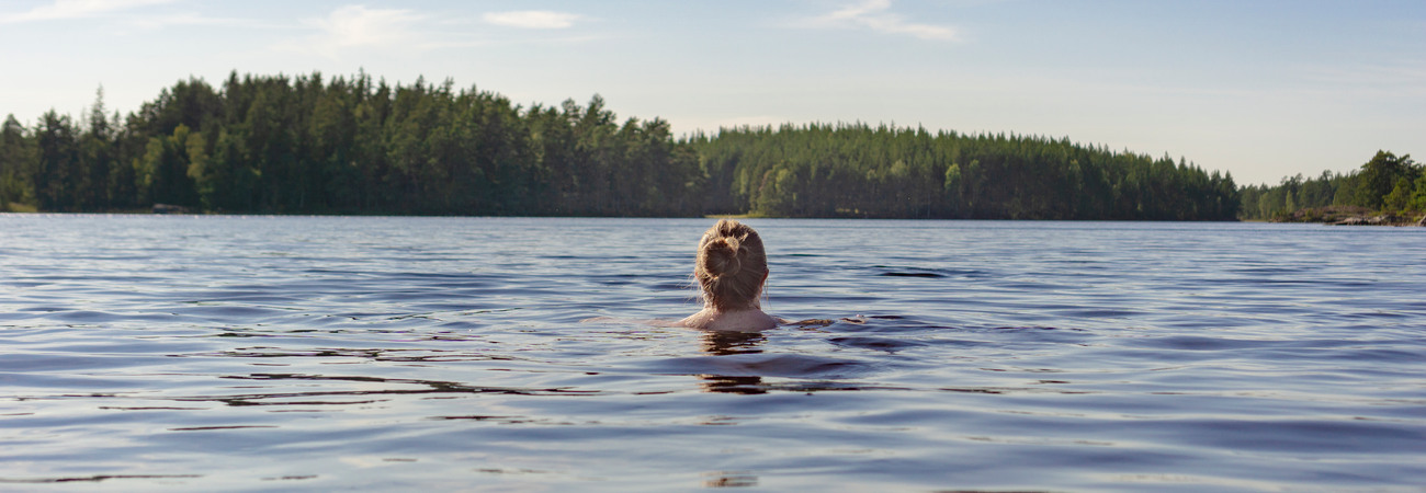 En person som simmar i en sjö med skog i bakgrunden.