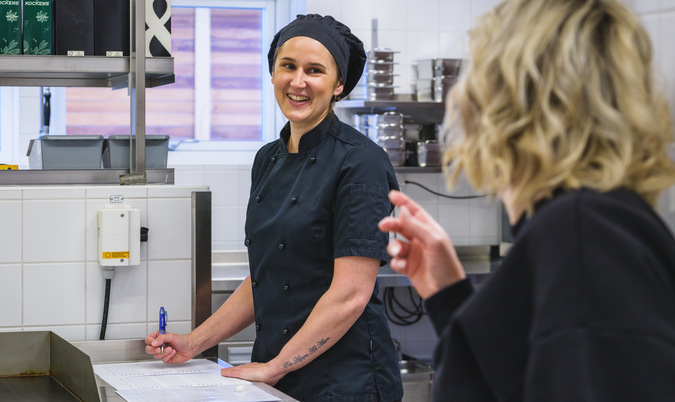 Fotot visar två kvinnor klädda i svart. De är i köksmiljö för måltidsservice i Finspångs kommun.